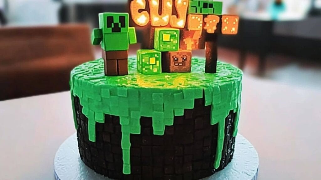 A Minecraft-themed birthday cake featuring green slime dripping over a block-like black base, with figurines of a Creeper, glowing letters spelling "CUTE," and Minecraft blocks on top.