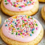 Soft sugar cookies topped with swirls of pink frosting and colorful sprinkles, arranged on a baking tray, Does Crumbl throw away cookies at the end of the day?