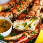 Fresh crab legs garnished with parsley, drizzled with melted butter, and served with lemon wedges and a ramekin of butter sauce.