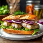 A traditional Matjes herring recipe featuring pickled herring fillets, red onions, and fresh lettuce in a crispy bread roll, garnished with dill.