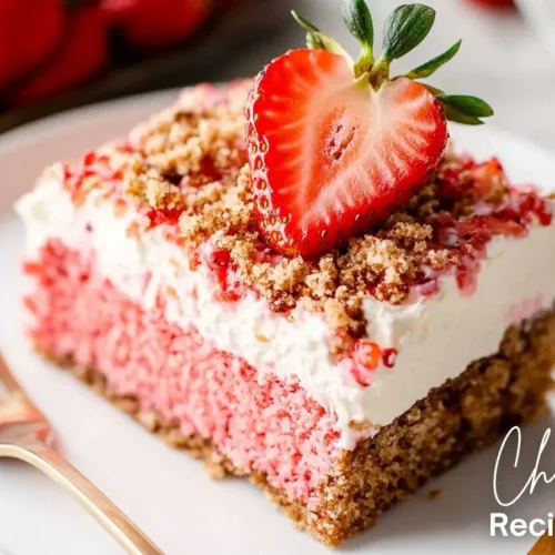 A slice of homemade strawberry crunch cake recipe with a golden brown crust, topped with whipped frosting, crunchy crumble, and a fresh strawberry half.